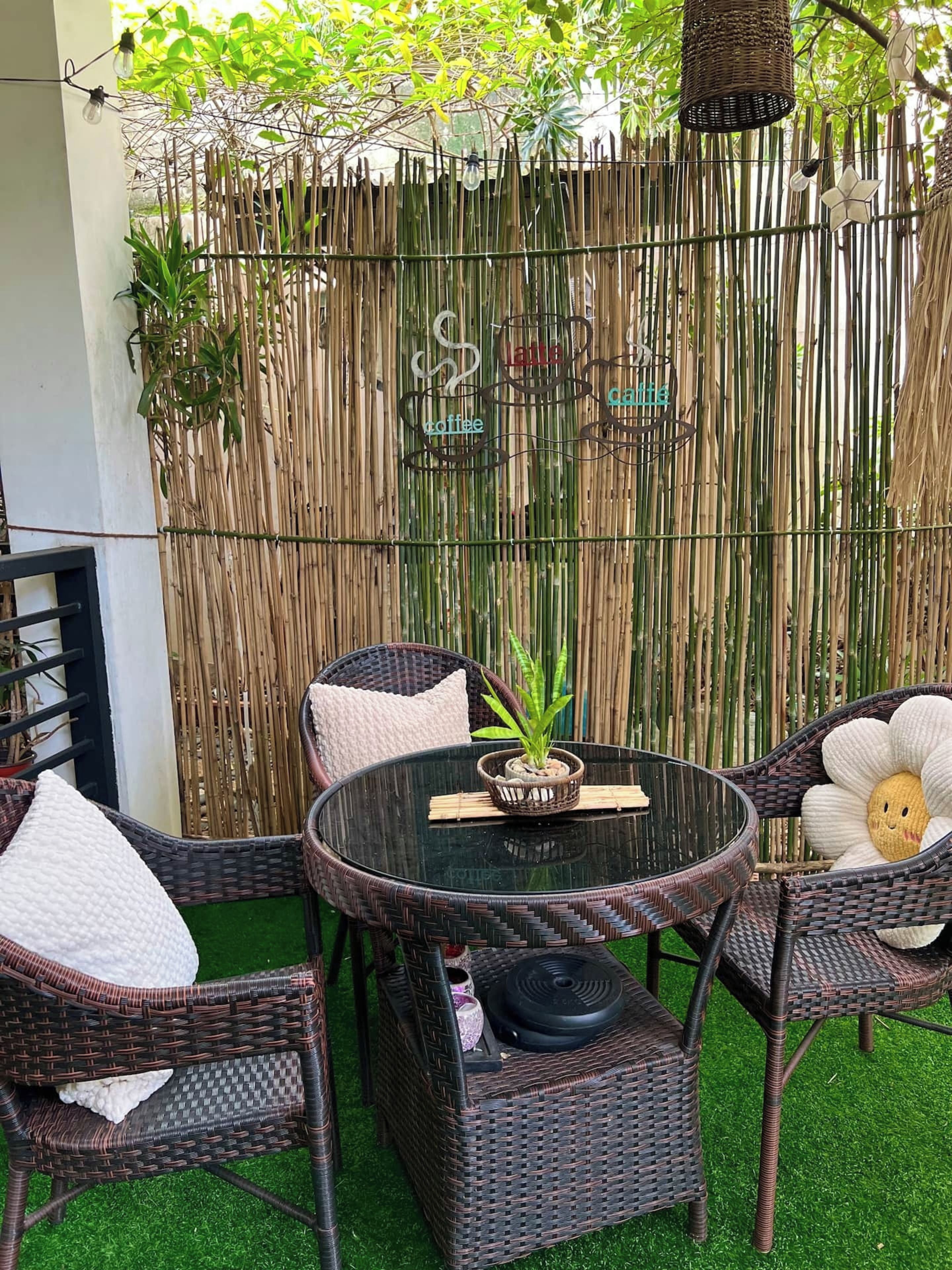 A round glass table with wicker chairs, a potted plant, and a decorative item in the center.