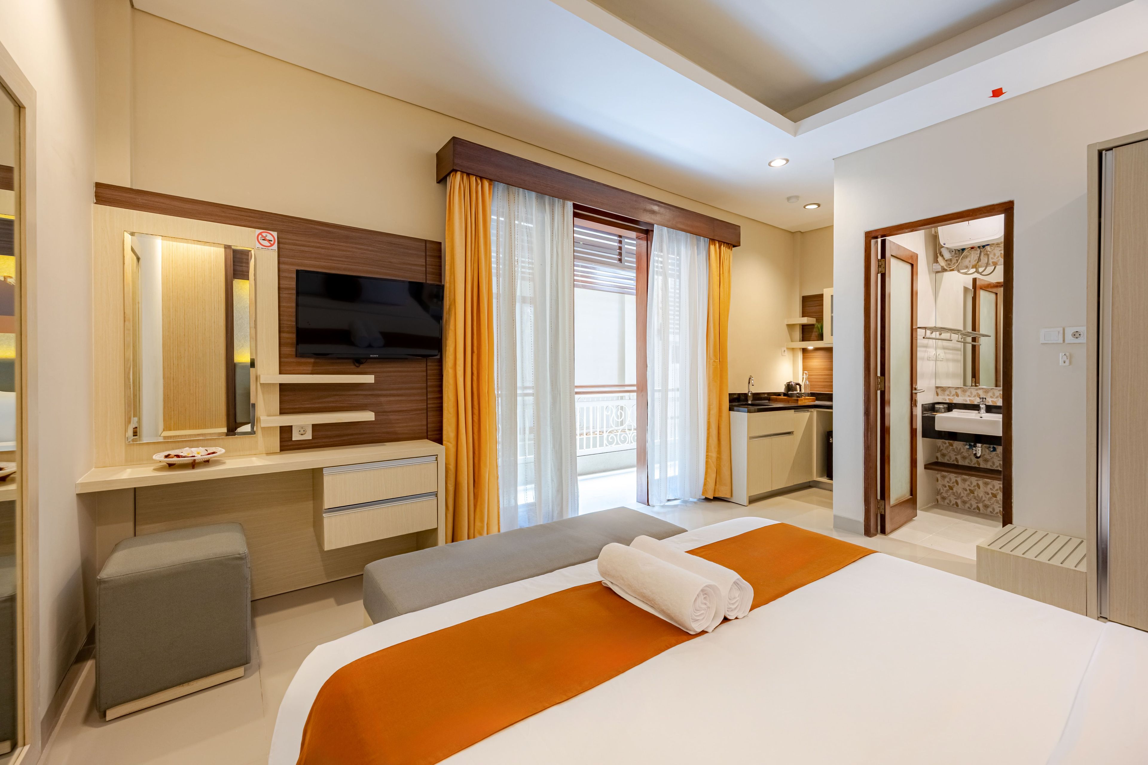 Habitación de hotel con cama, televisor, escritorio, baño y balcón.