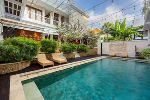 A swimming pool with lounge chairs, surrounded by greenery and a stone wall. - Cove Rumah Padi (Kabupaten Badung)