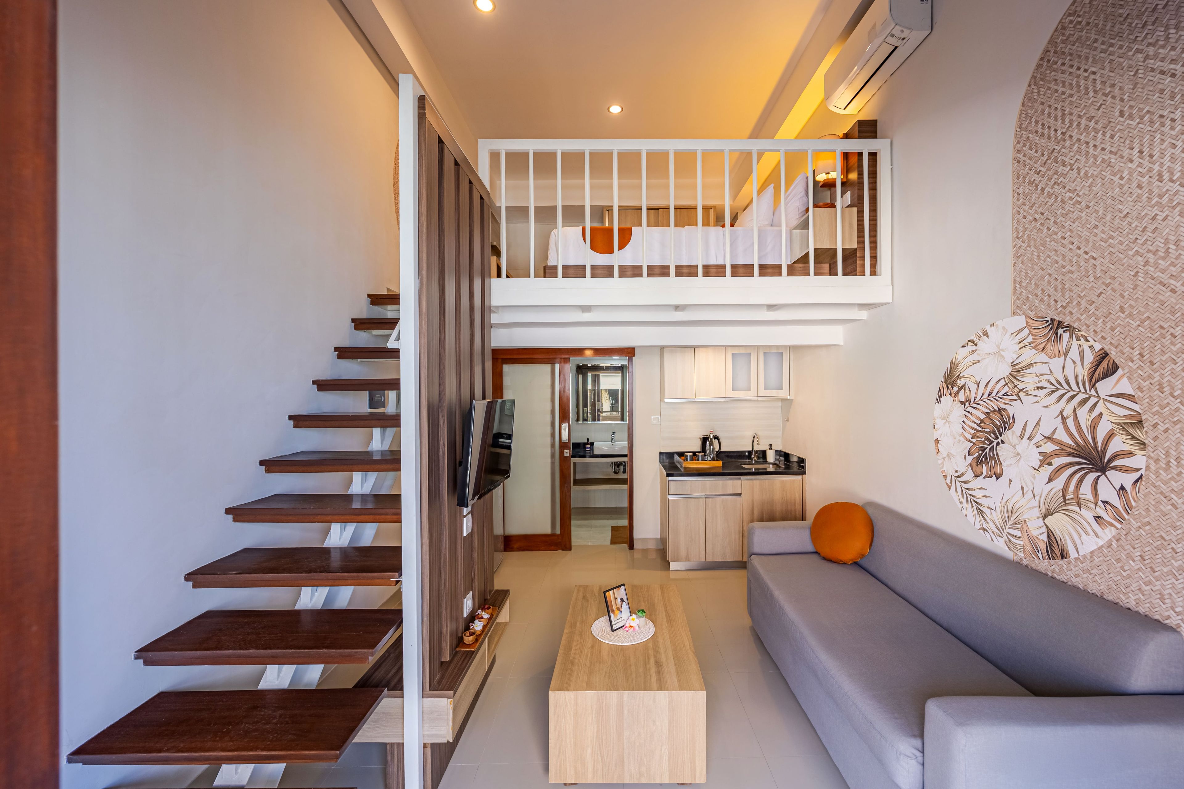 Un apartamento moderno con una escalera que conduce a un dormitorio tipo loft, una zona de cocina y una sala de estar con sofá y mesa de centro.