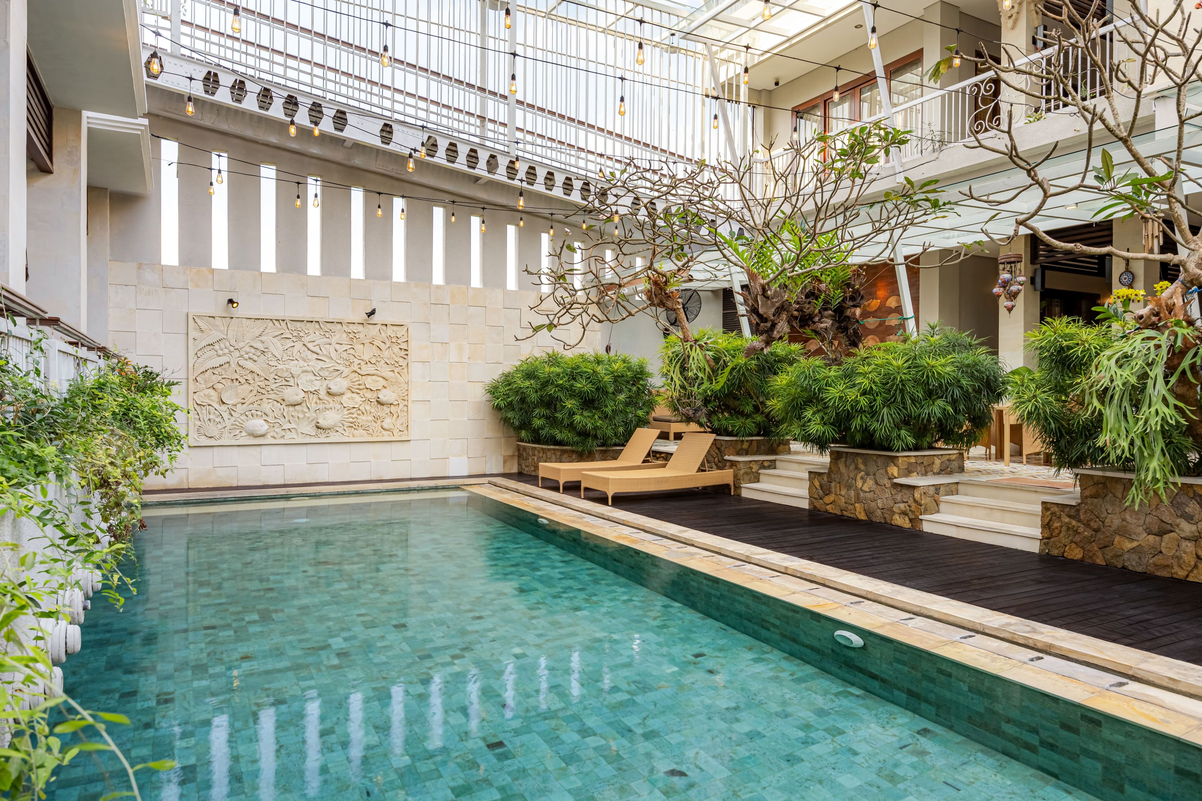 A pool area with clear water, lounge chairs, and a decorative wall with carvings.