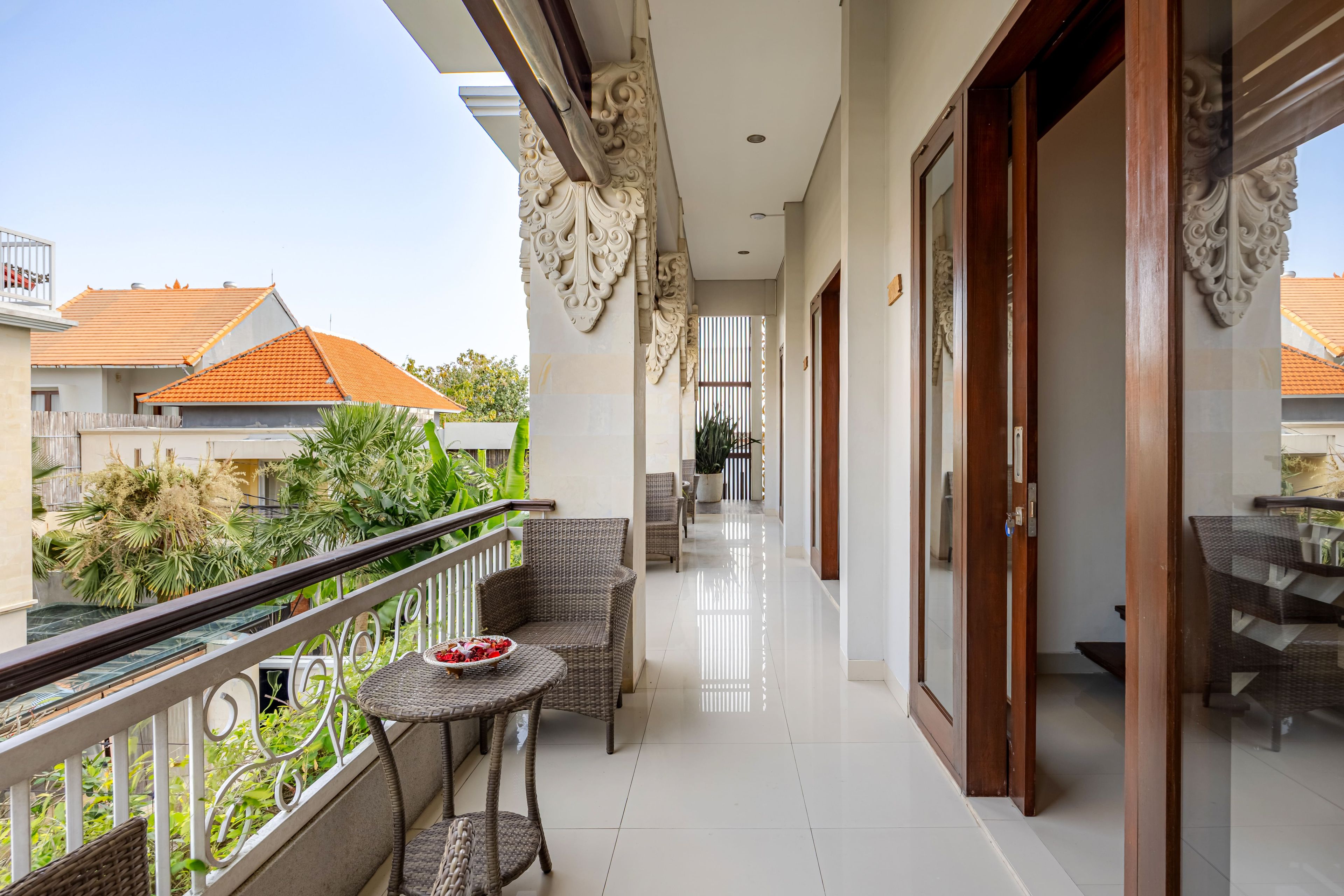 Un balcón con muebles de mimbre, una pequeña mesa con un cuenco, y vistas a casas vecinas.