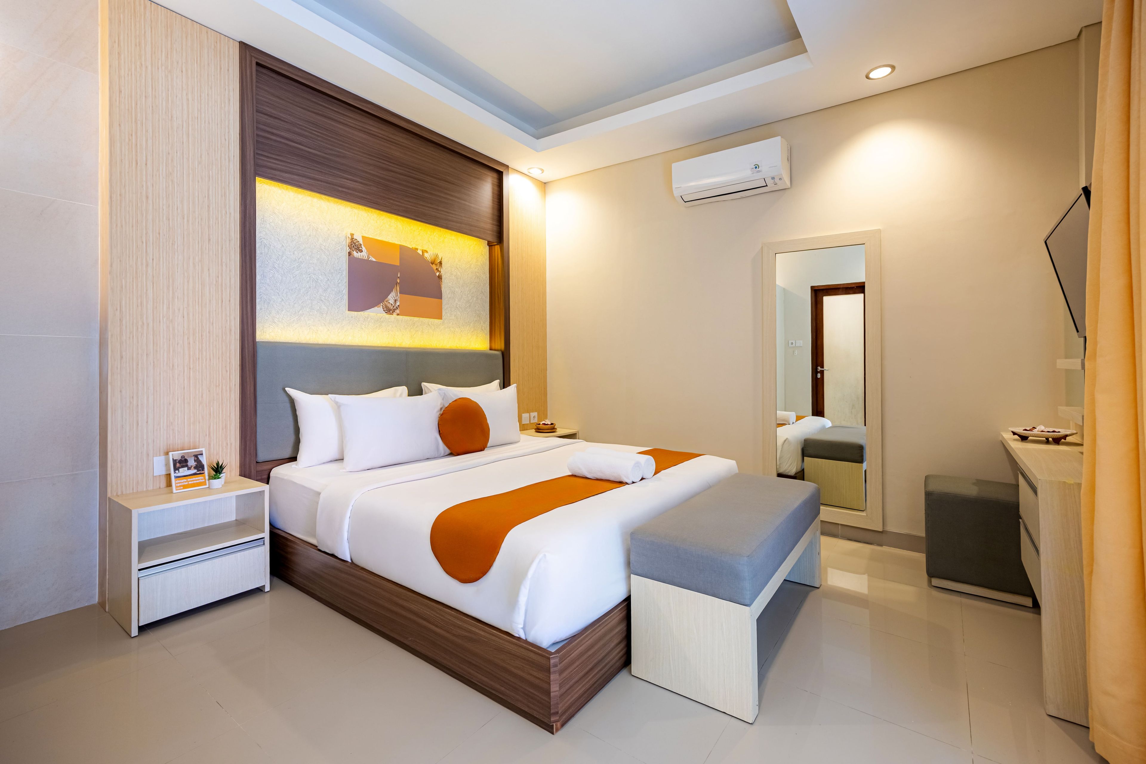 Una habitación de hotel moderna con una cama grande, una mesita de noche, un espejo y un equipo de aire acondicionado instalado en la pared.