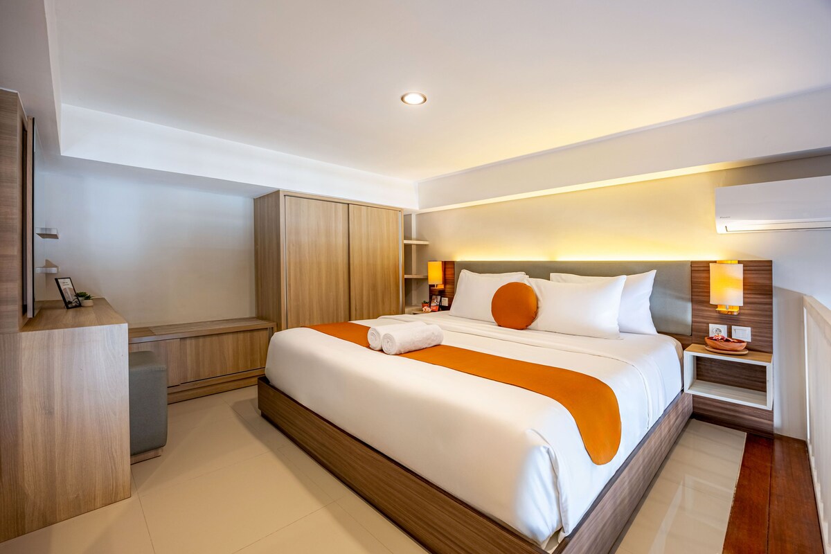A hotel room with a large bed, bedside tables, a desk, and a wardrobe.