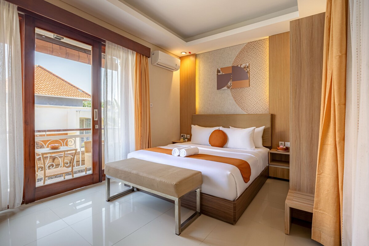 A hotel room with a bed, a bench, a small table, and a view of the outside.