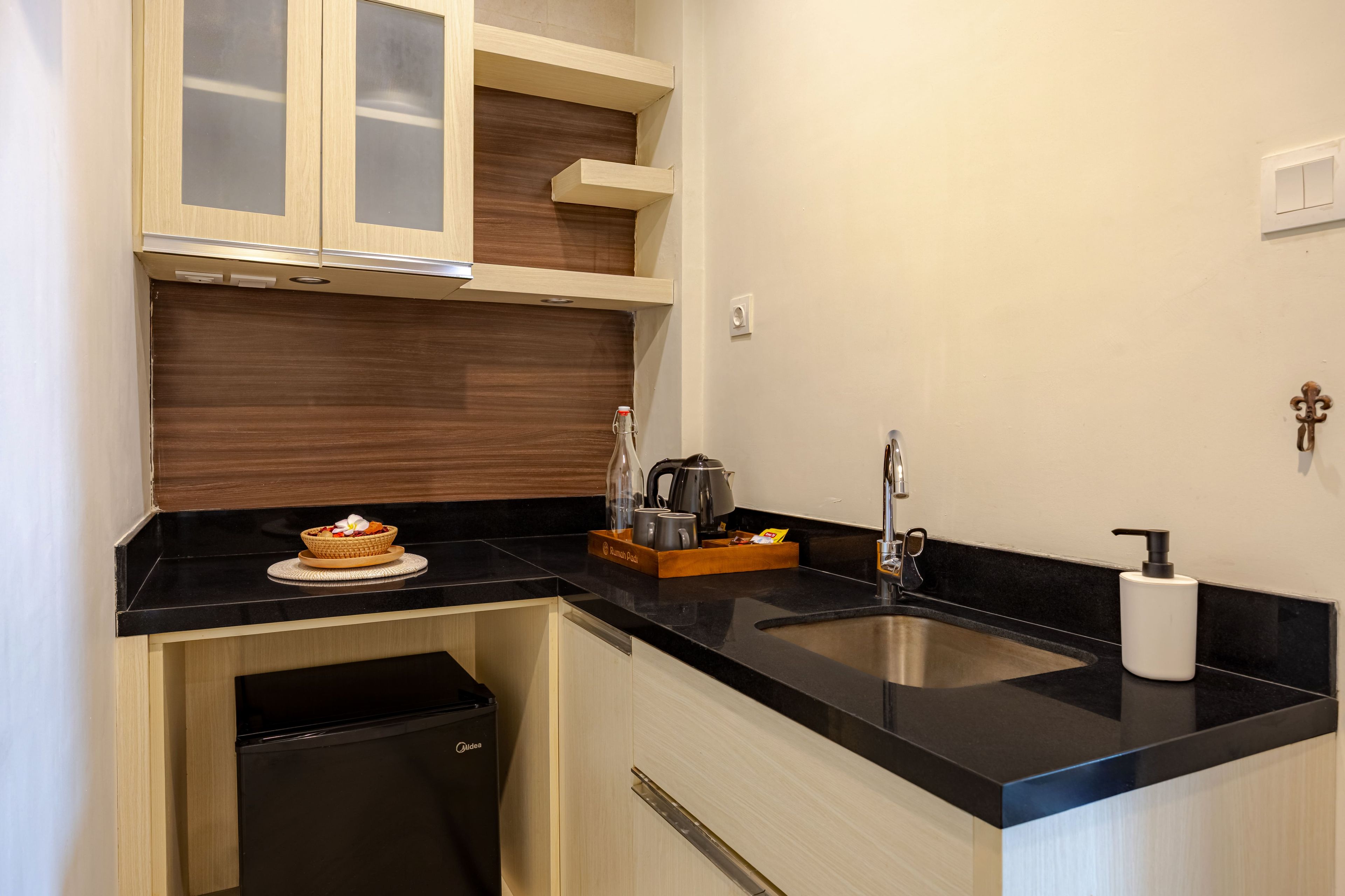 Una cocina compacta con encimera negra, armarios de madera, un lavamanos de acero inoxidable y un cubo de basura.