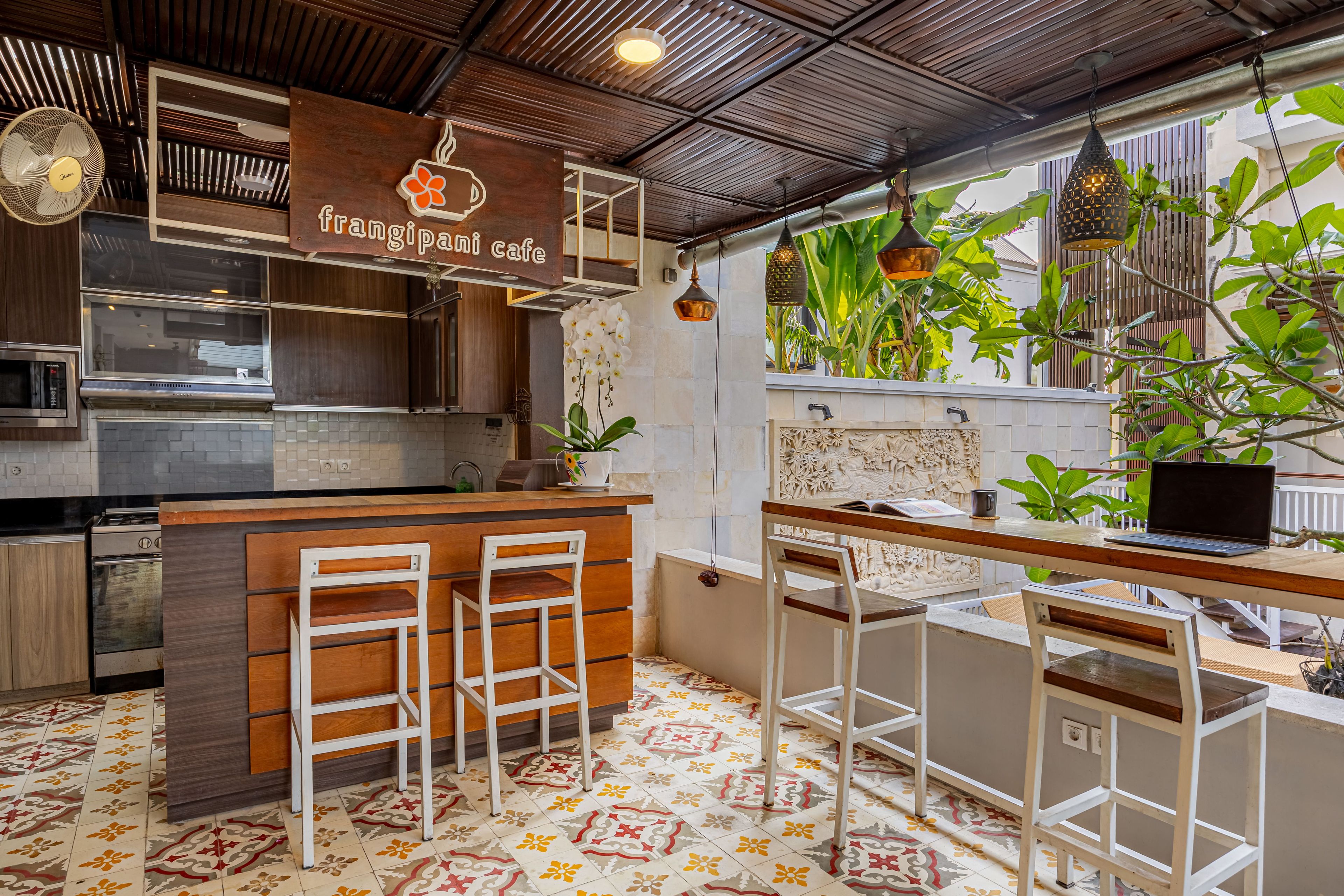 Interior de una cafetería con barra de madera, sillas blancas, suelo de baldosas y vistas a zonas verdes exteriores.