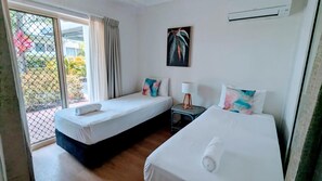 Una habitación de hotel con dos camas, una mesita, una lámpara y un cuadro en la pared.