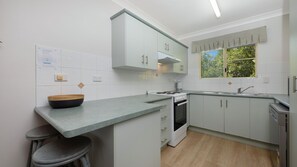 A modern kitchen with white cabinets, a grey countertop, a stove, and a window with a view of greenery.