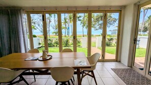 Un comedor con vistas al mar, una mesa con sillas y una ventana que ofrece vistas a palmeras y un área verde.