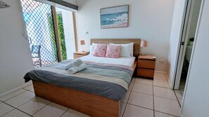Een slaapkamer met een bed, nachtkastjes, een schilderij en uitzicht door een raam.