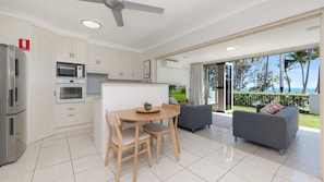 A modern kitchen with white cabinets, a dining area with a wooden table and chairs, and a balcony with a view of the ocean.