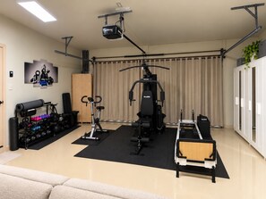 A home gym with exercise equipment, a projector, and a wall-mounted TV. - Redlands Retreat Pool + Volleyball Sleeps 10 (Miami)