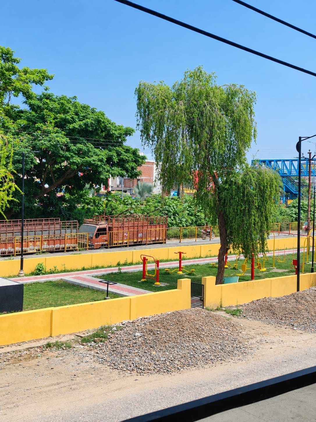 Un parque infantil con equipo de ejercicio, una valla amarilla y un árbol.