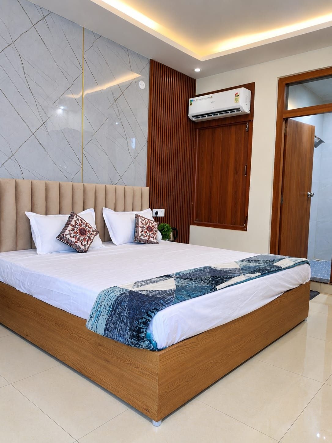 Un dormitorio moderno con una cama grande, cabecera de madera, pared de mármol y un equipo de aire acondicionado.
