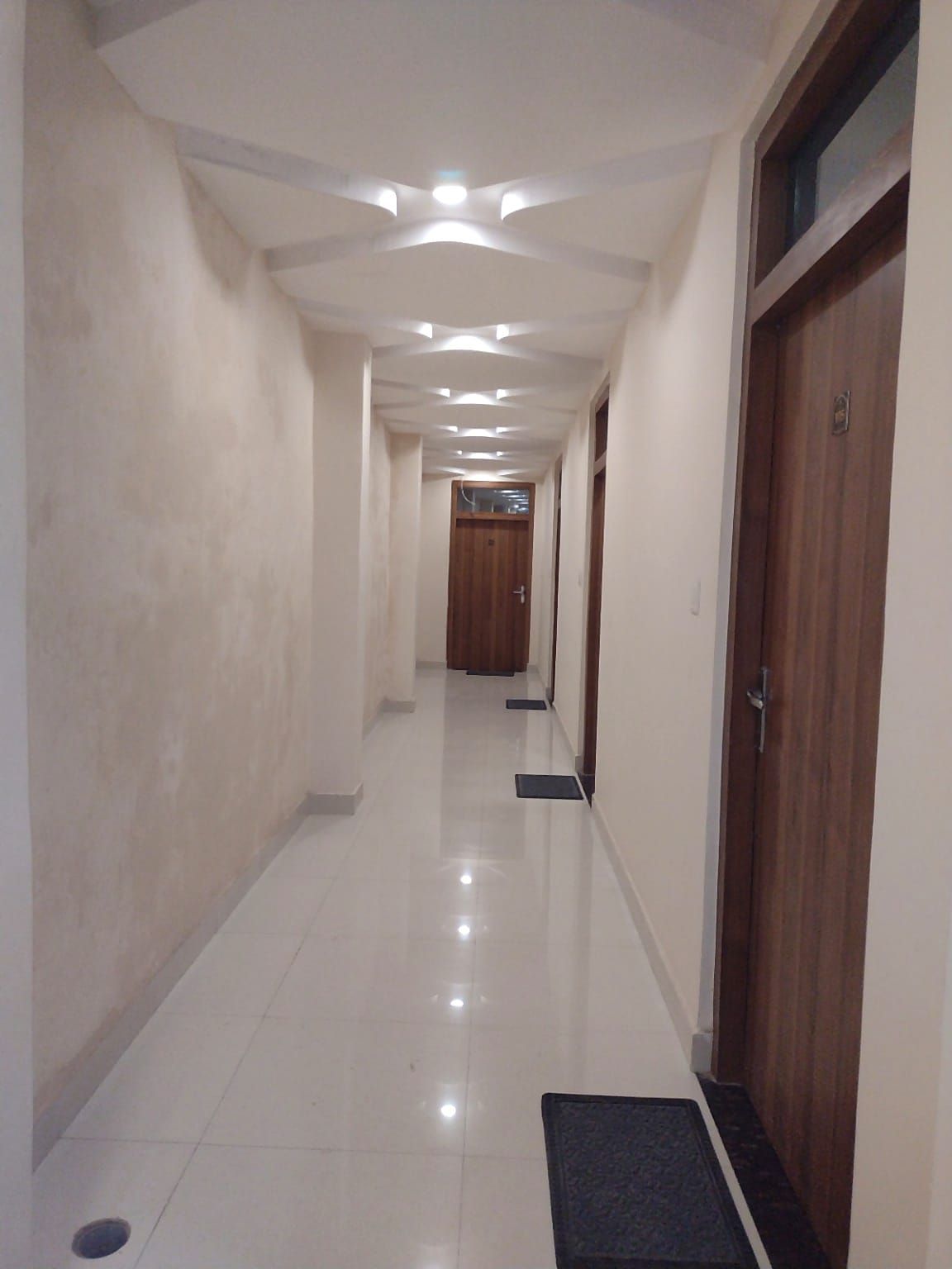 Un pasillo con piso pulido, iluminación empotrada y puertas de madera.