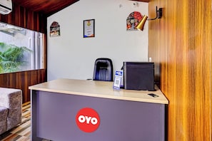 Una recepción con un logotipo 'OYO', un certificado enmarcado, una silla de oficina negra, una lámpara de escritorio y una pequeña mesa con un teléfono móvil.