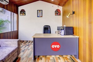 A reception desk with a logo, a chair, a desk lamp, and a plant. - Super Hotel O Oxygen (Samudrapur)