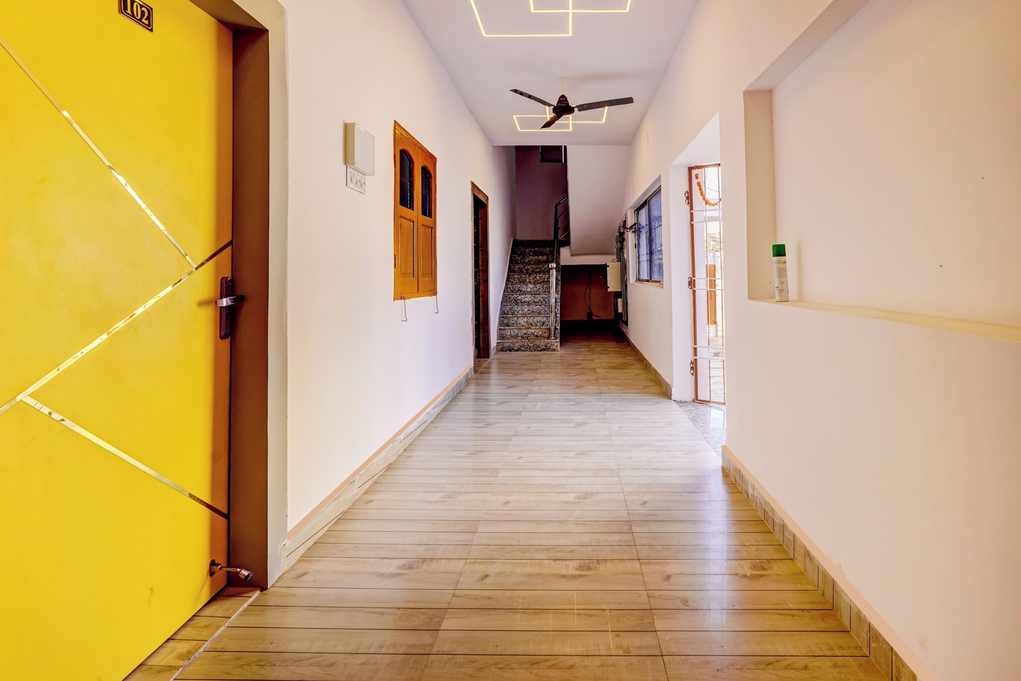 A hallway with a wooden floor, a ceiling fan, and a staircase leading to another level.
