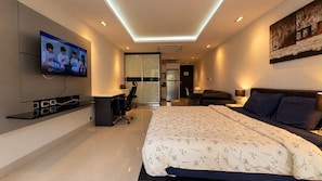 Habitación de hotel moderna con una cama grande, un escritorio, un televisor y una puerta de vidrio que da a una kitchenette.