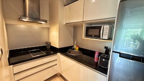 Una cocina compacta con campana de acero inoxidable, microondas, tostadora y un lavamanos.