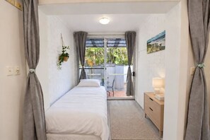 A small, single-bed room with a view of a garden through a sliding door. - Stylish 2BR Home | Parking & Courtyard (Ashfield)