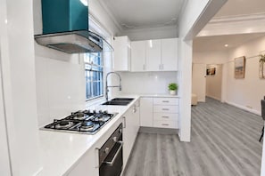 A modern kitchen with white cabinets, a gas stove, and a window. - Stylish 2BR Home | Parking & Courtyard (Ashfield)