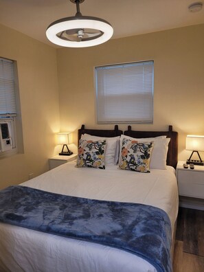 A bedroom with a bed, two bedside lamps, a ceiling light, a window with blinds, and an air conditioning unit. - Quiet Studio · Free Parking (Hollywood)