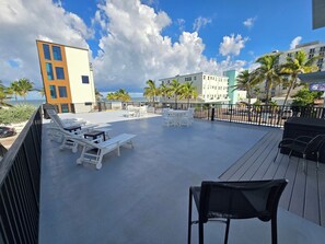 A rooftop terrace with lounge chairs and tables, overlooking a beach and palm trees. - Quiet Studio · Free Parking (Hollywood)