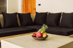 A modern living room with a wooden coffee table in the foreground and a black sofa with matching cushions in the background. - Villa Malika – A Private Haven in the Tropics (Maret)