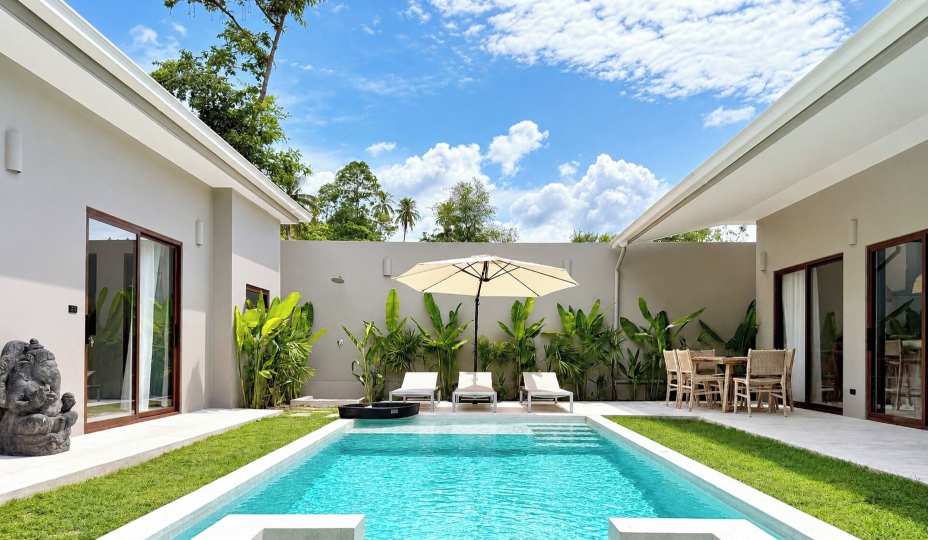 A modern pool area with a clear blue pool, surrounded by lush greenery and a white wall.