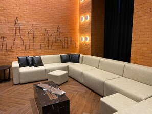 Een moderne woonkamer met een hoekbank, een salontafel en een bakstenen muur met een stadsgezichtsmural.