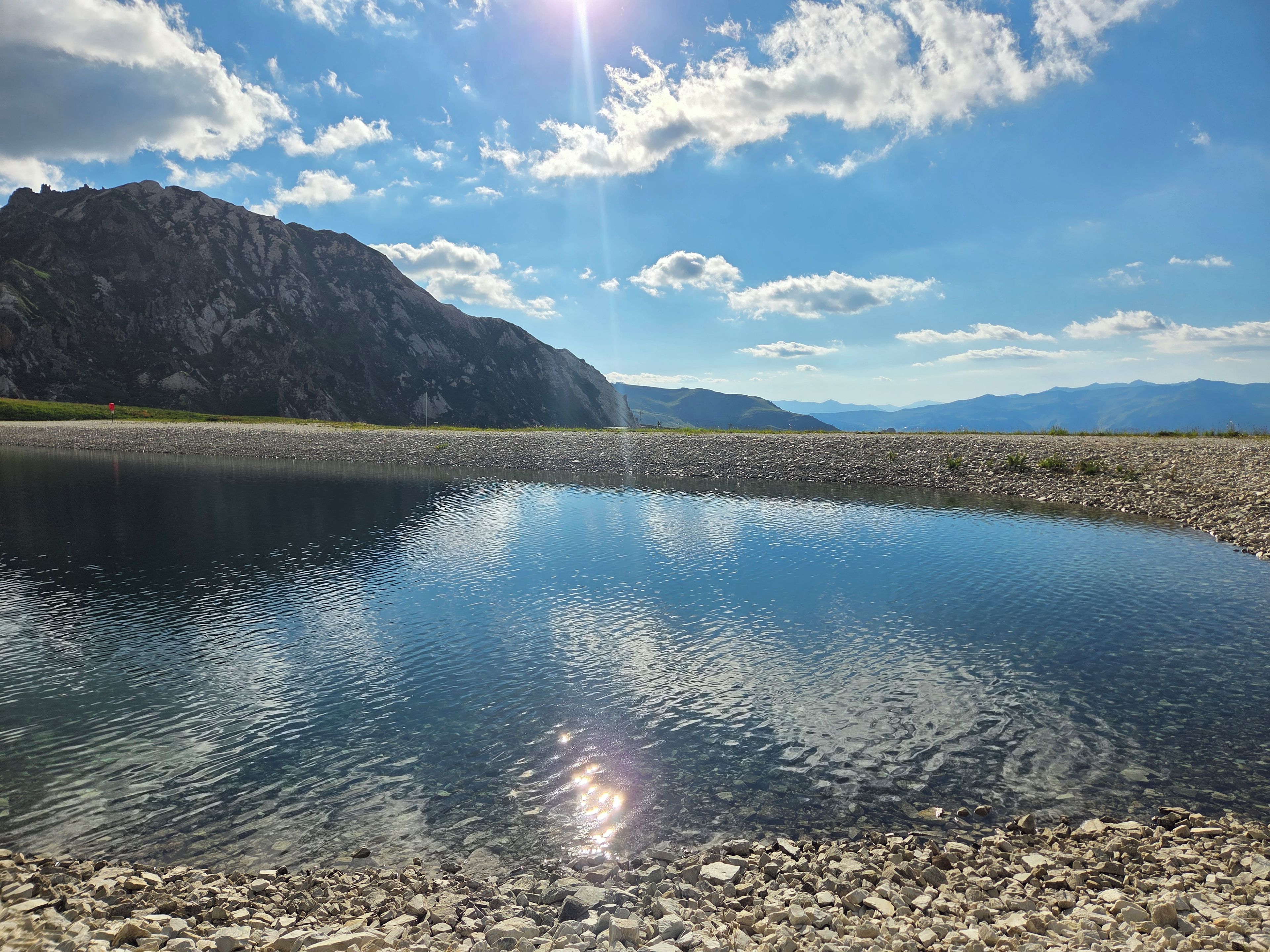 A clear lake with a rocky shoreline and mountains in the background.