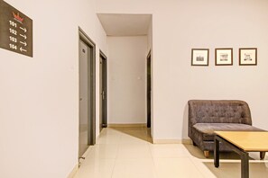 Un pasillo de hotel con un sofá, una mesa, un cartel con números de habitación y cuadros en la pared.