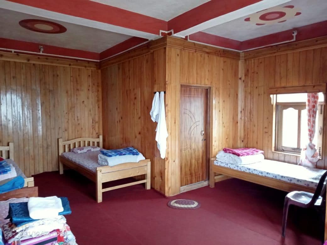 A room with wooden walls, two beds, a wardrobe, and a window with curtains.