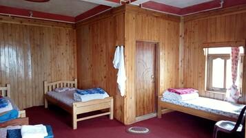 A room with wooden walls, two beds, a wardrobe, and a window with curtains.