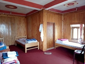 Ein Zimmer mit Holzwänden, zwei Betten, einem Kleiderschrank und einem Fenster mit Vorhängen.