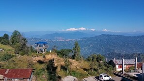 A mountainous landscape with a clear sky, a blue-roofed structure, and a white van parked on the roadside. - PARIJAT HOMESTAY (Lulagaon Khasmahal,Kalimpong)