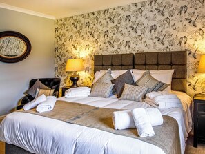 A neatly made bed with pillows and a folded towel, a round mirror on the wall, and a floral wallpaper pattern. - 8 bedroom accommodation in Aboyne (Aboyne)