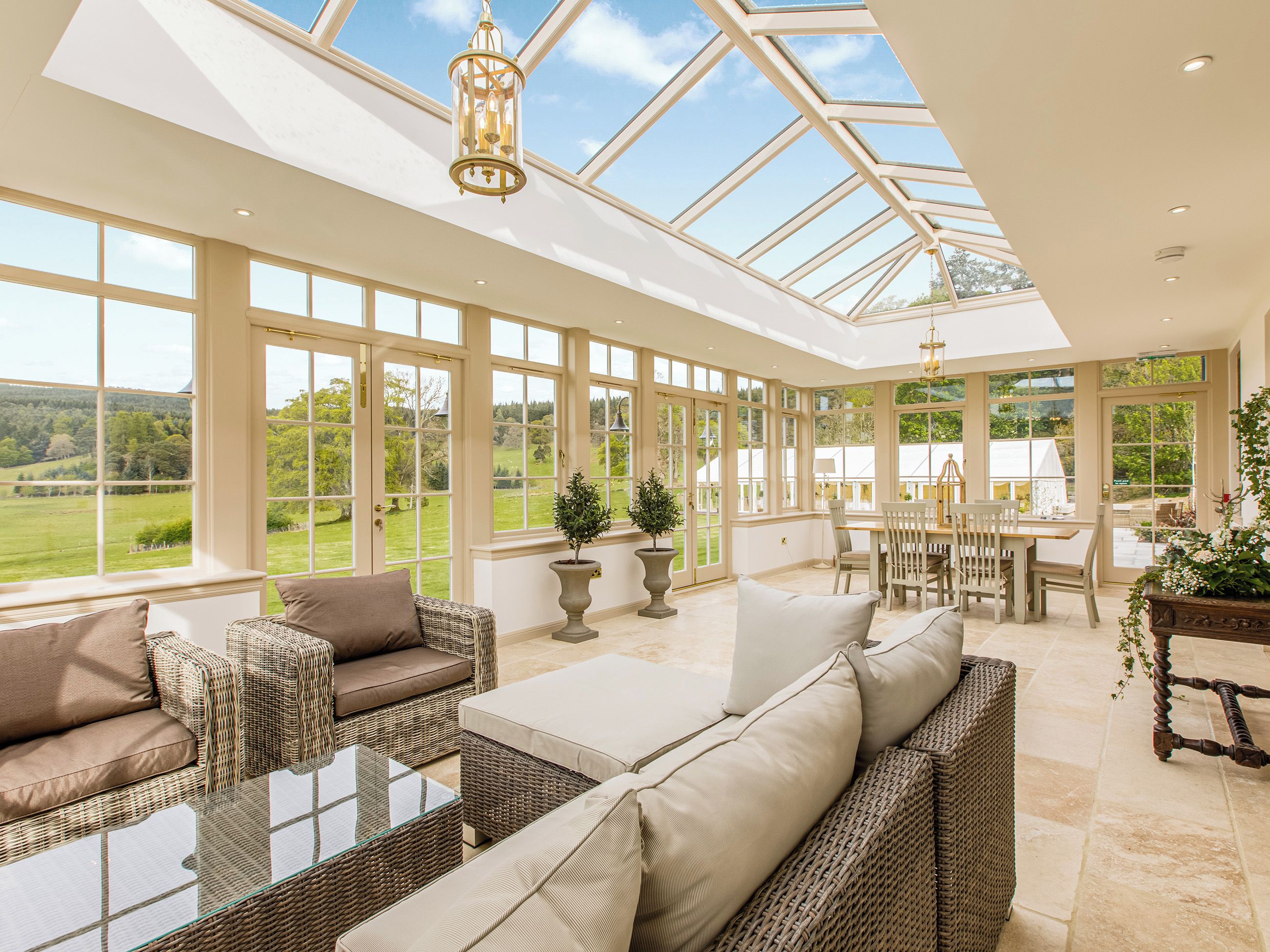 A conservatory with wicker furniture, a glass table, and a view of the countryside.