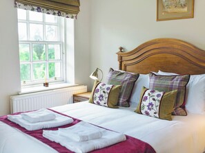 A neatly made bed with white linens and a red accent, a bedside lamp, and a window with a view of greenery. - 8 bedroom accommodation in Aboyne (Aboyne)