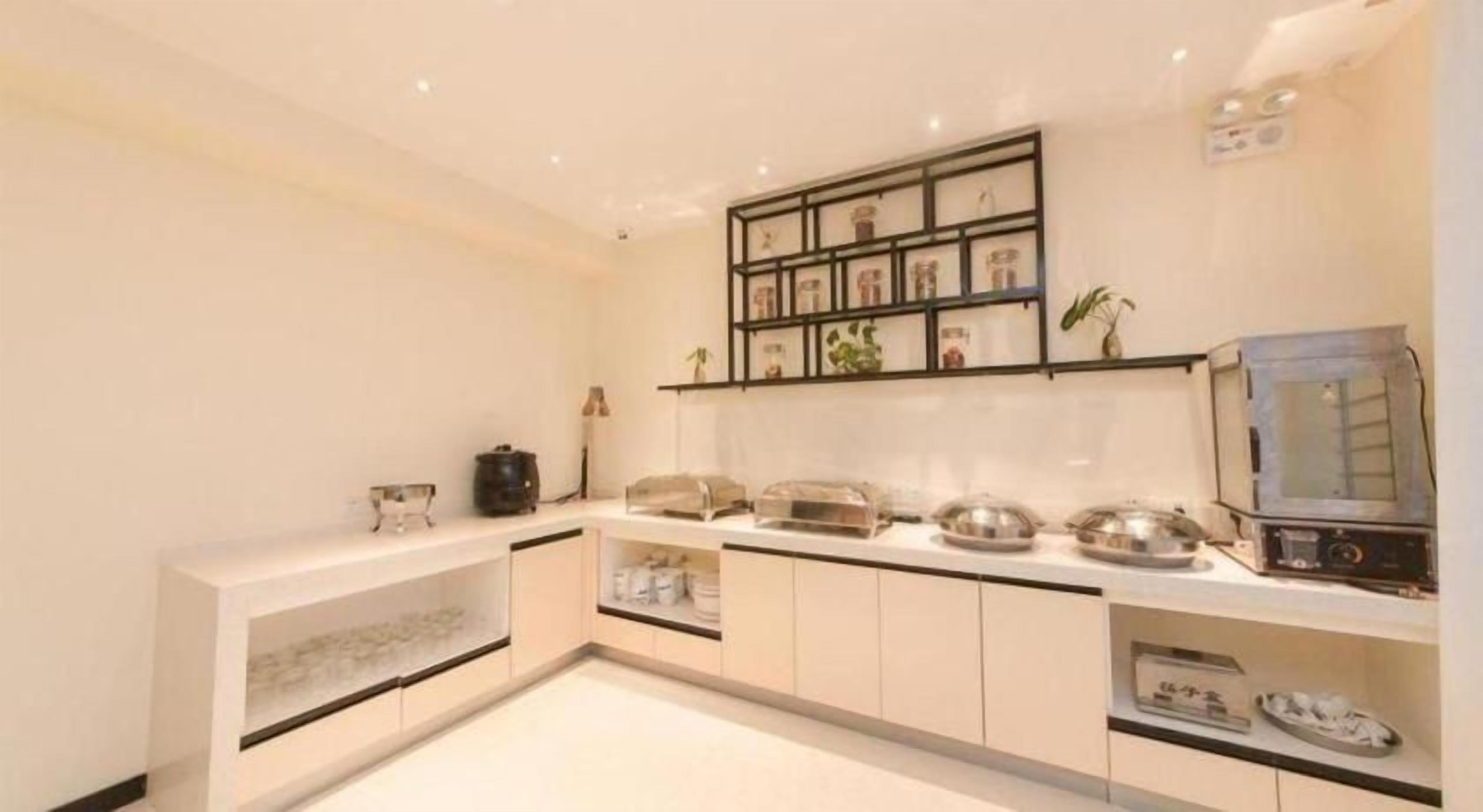 A modern kitchen with white cabinetry, a built-in oven, and a microwave. There is a shelf with decorative items and a small plant.