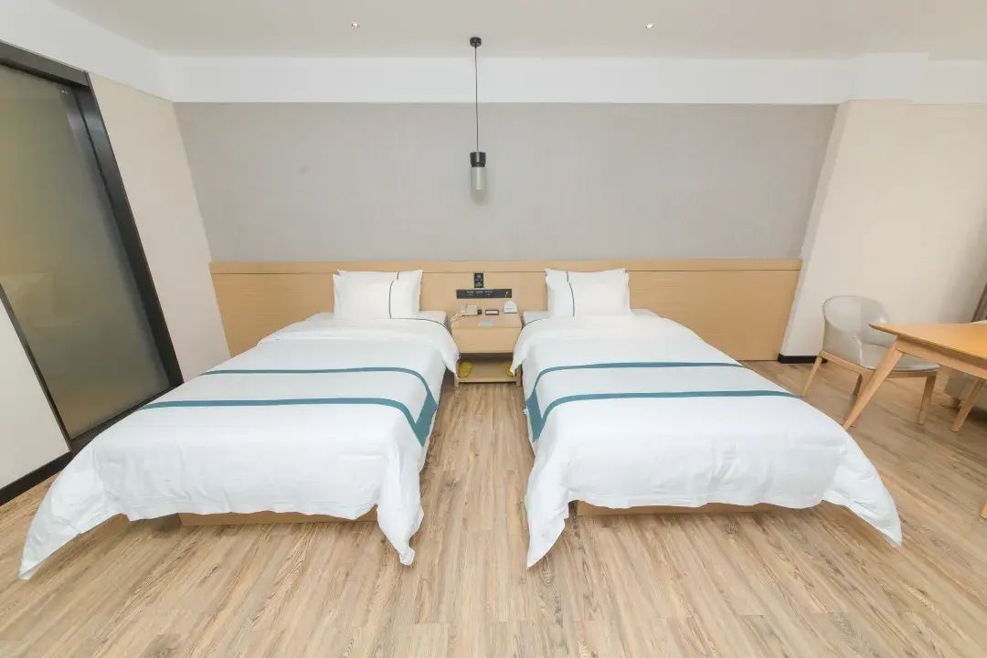 A hotel room with two single beds, a wooden headboard, a desk, and a chair.