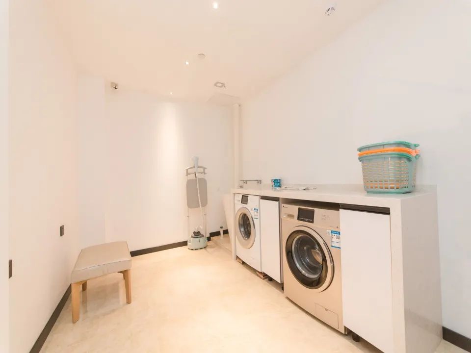 A laundry room with two washing machines, a drying rack, and a bench.