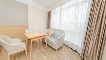 Una habitación de hotel moderna con suelo de madera, un sofá color beige, un sillón blanco y una pequeña mesa de madera.