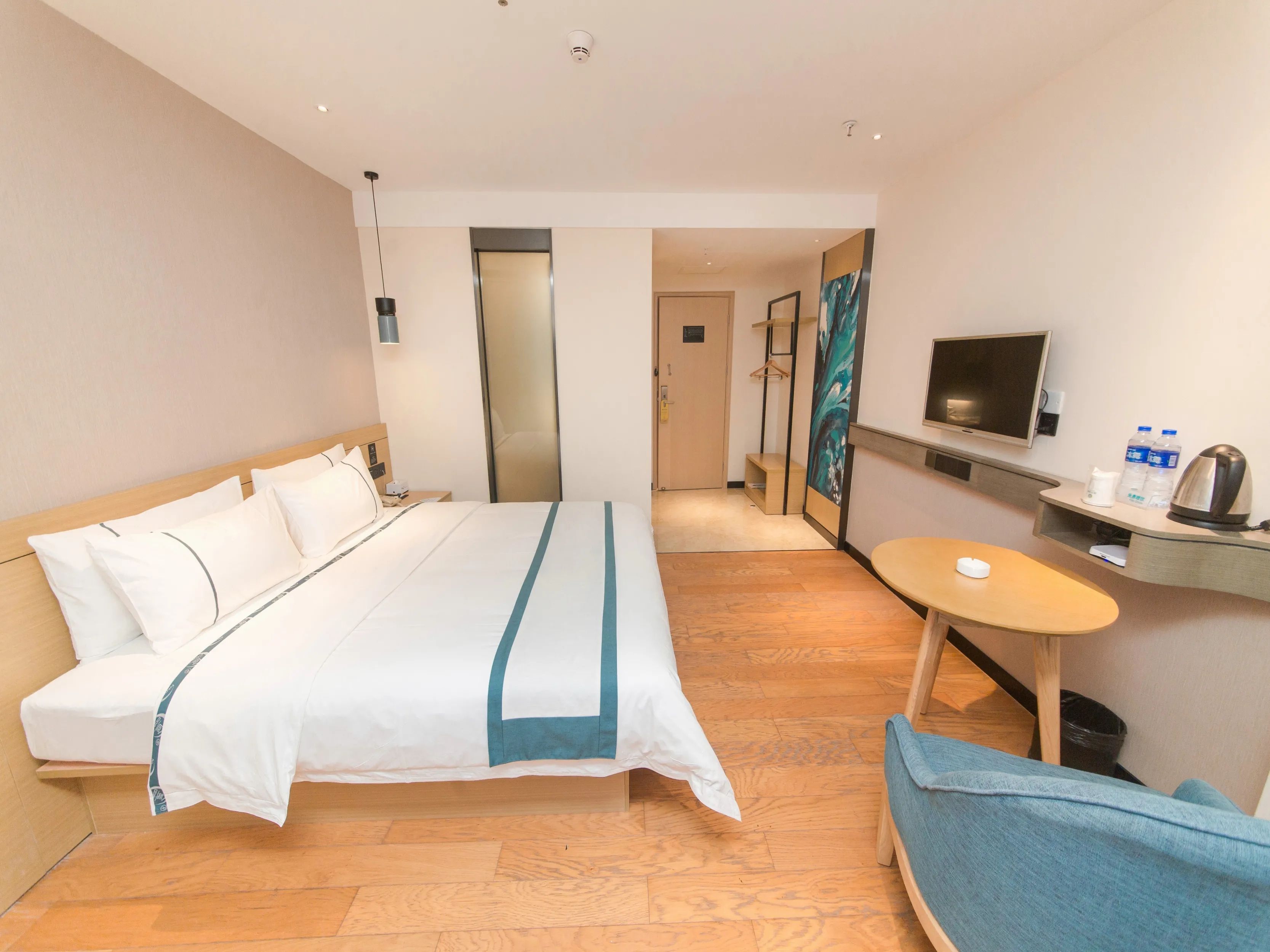 A hotel room with a bed, a desk with a chair, a television, and a small table.