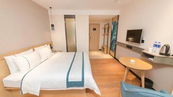 A hotel room with a bed, a desk with a chair, a television, and a small table.