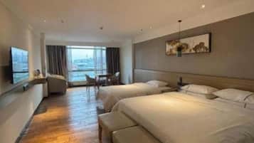 Habitación de hotel con dos camas, un sofá, un televisor y un ventanal con vistas a la ciudad.