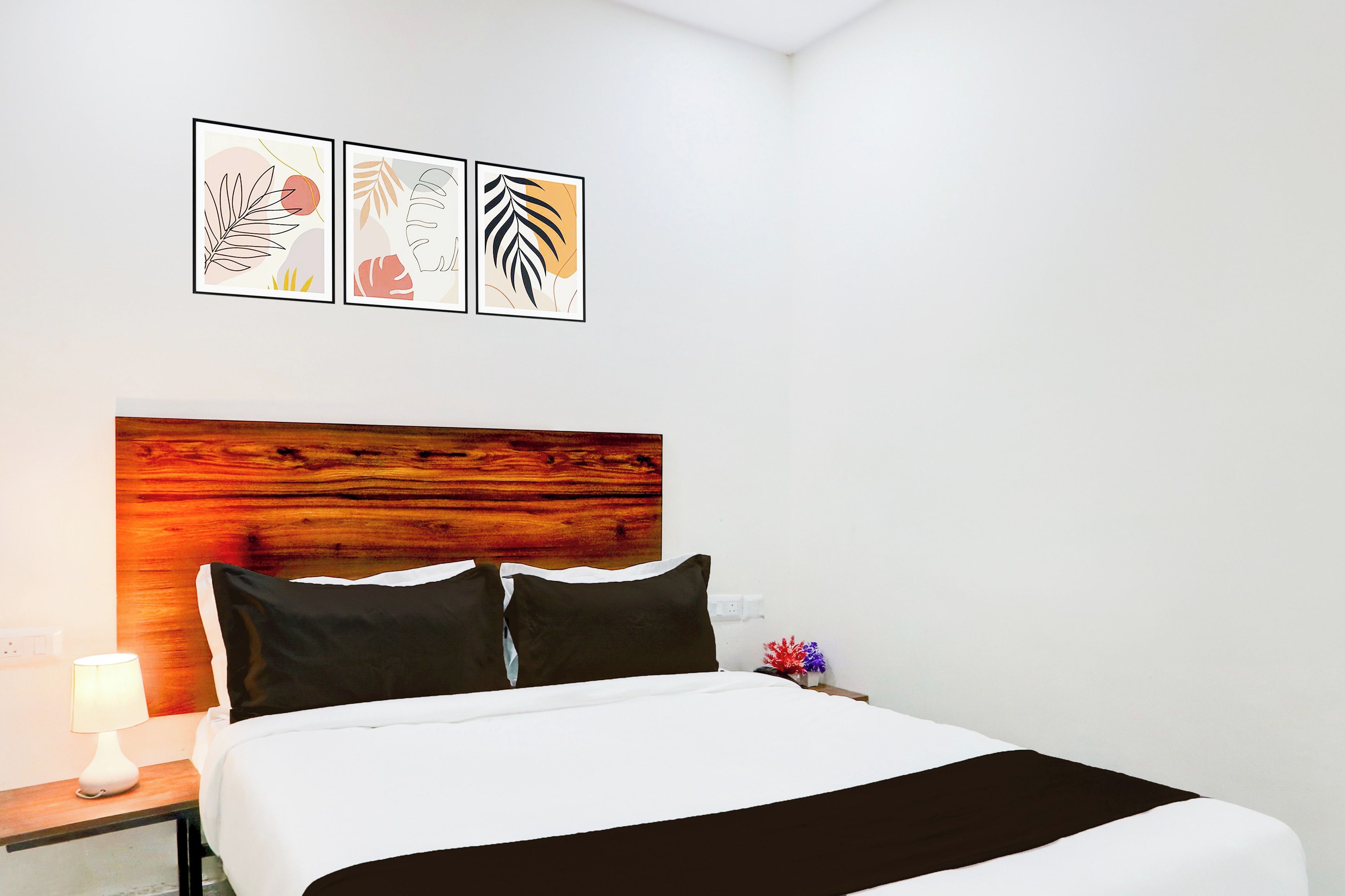 Una habitación de hotel con cama, mesita de noche, lámpara y tres cuadros en la pared.