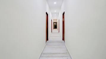 Un largo pasillo estrecho con paredes blancas y piso de mármol, que conduce a una puerta al final.